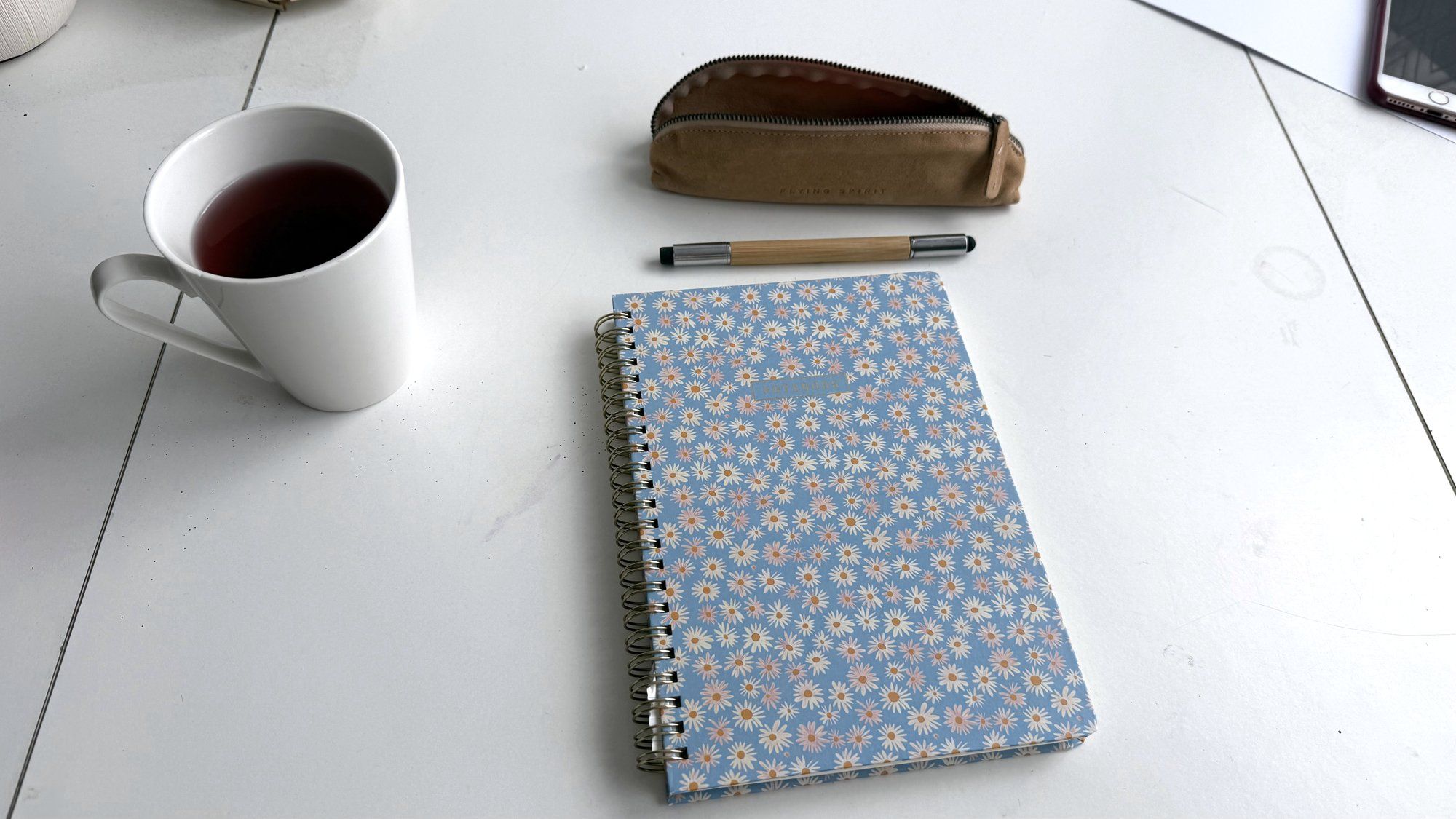 Un carnet fleuri, un stylo et une tasse posés sur une table