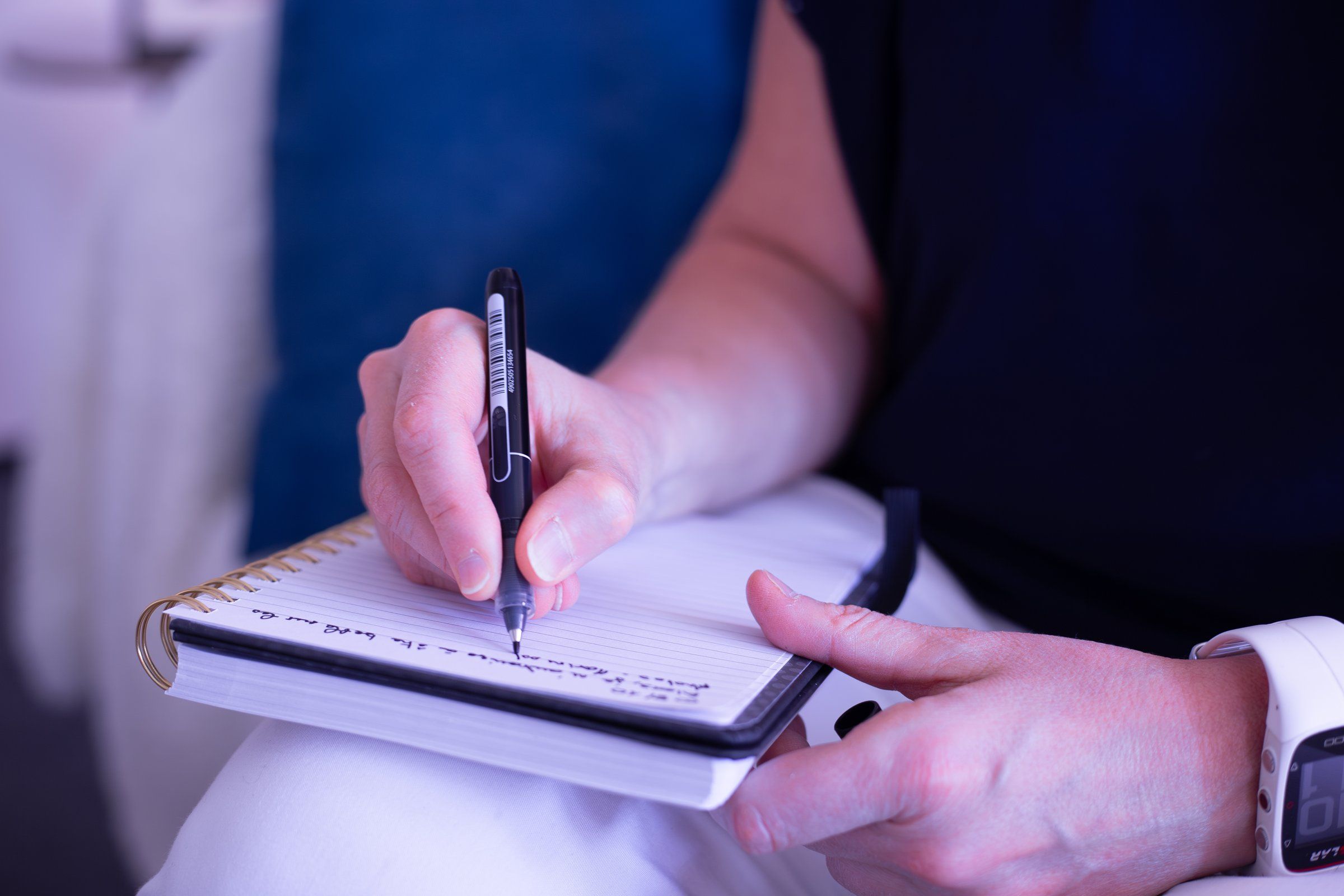 Une main écrit au stylo dans un carnet ouvert, pendant un travail de recherche de mots