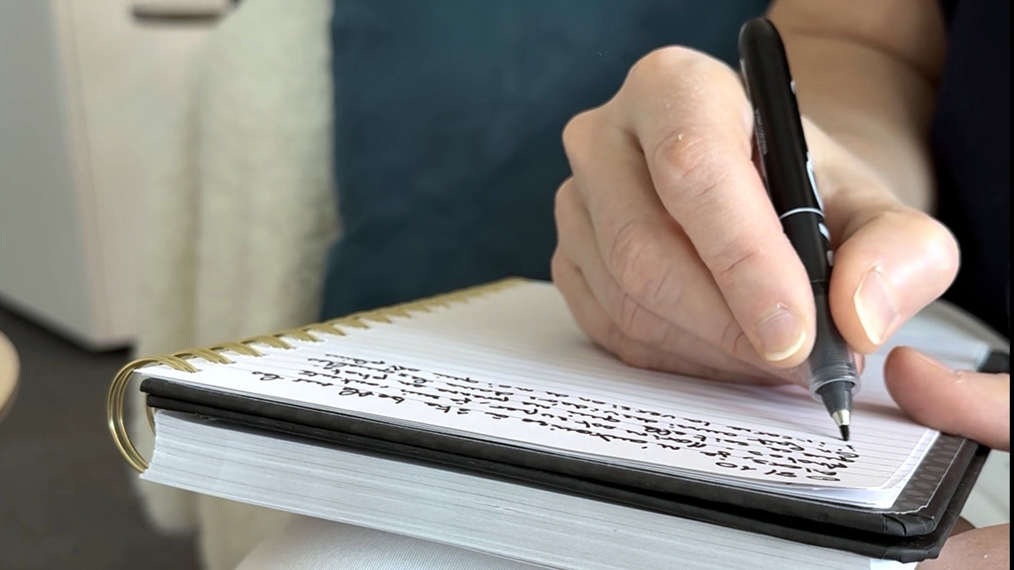 Une main écrit au stylo dans un carnet à spirale