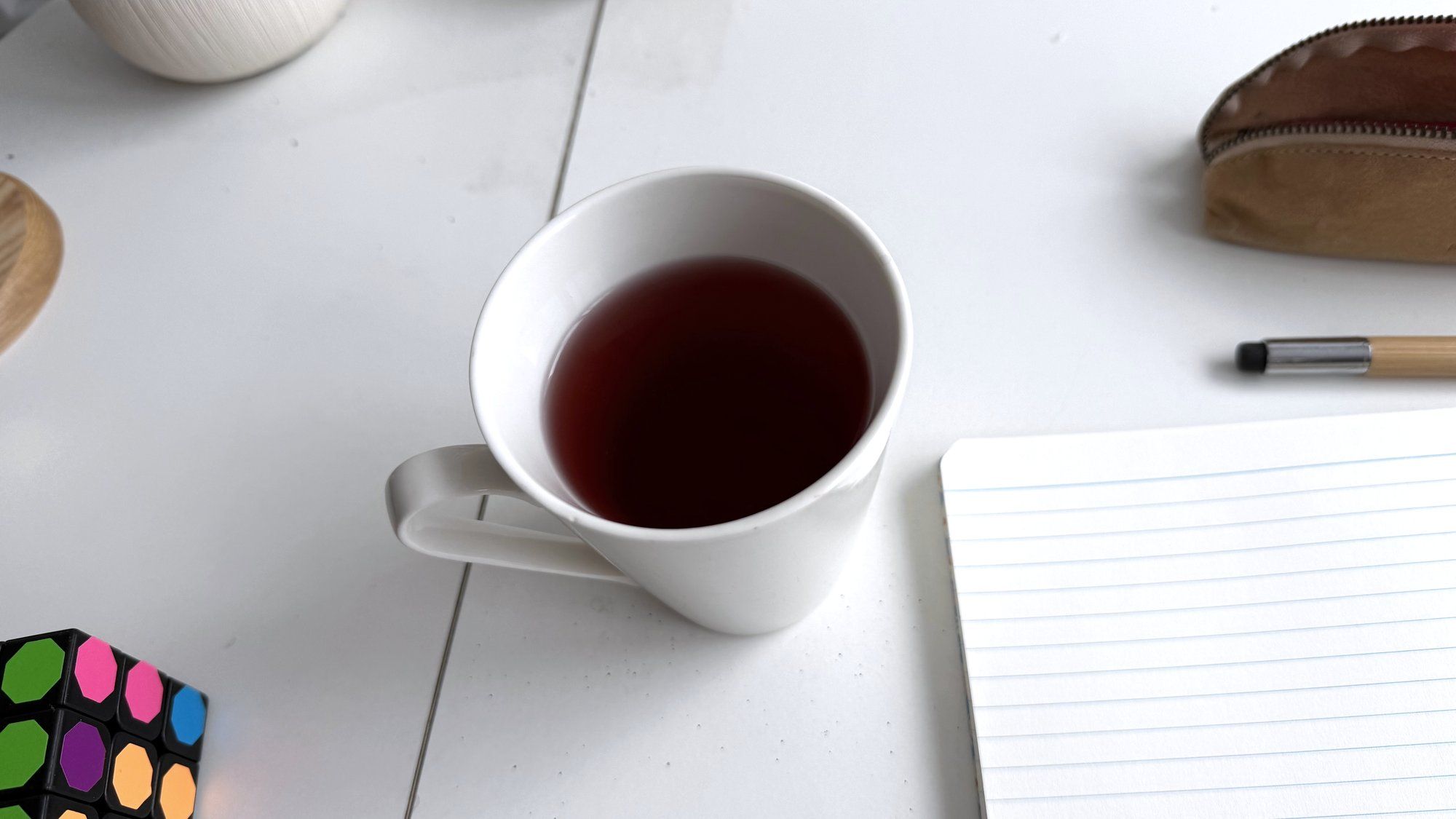 Une tasse de thé à côté d’un carnet ouvert, sur une table blanche
